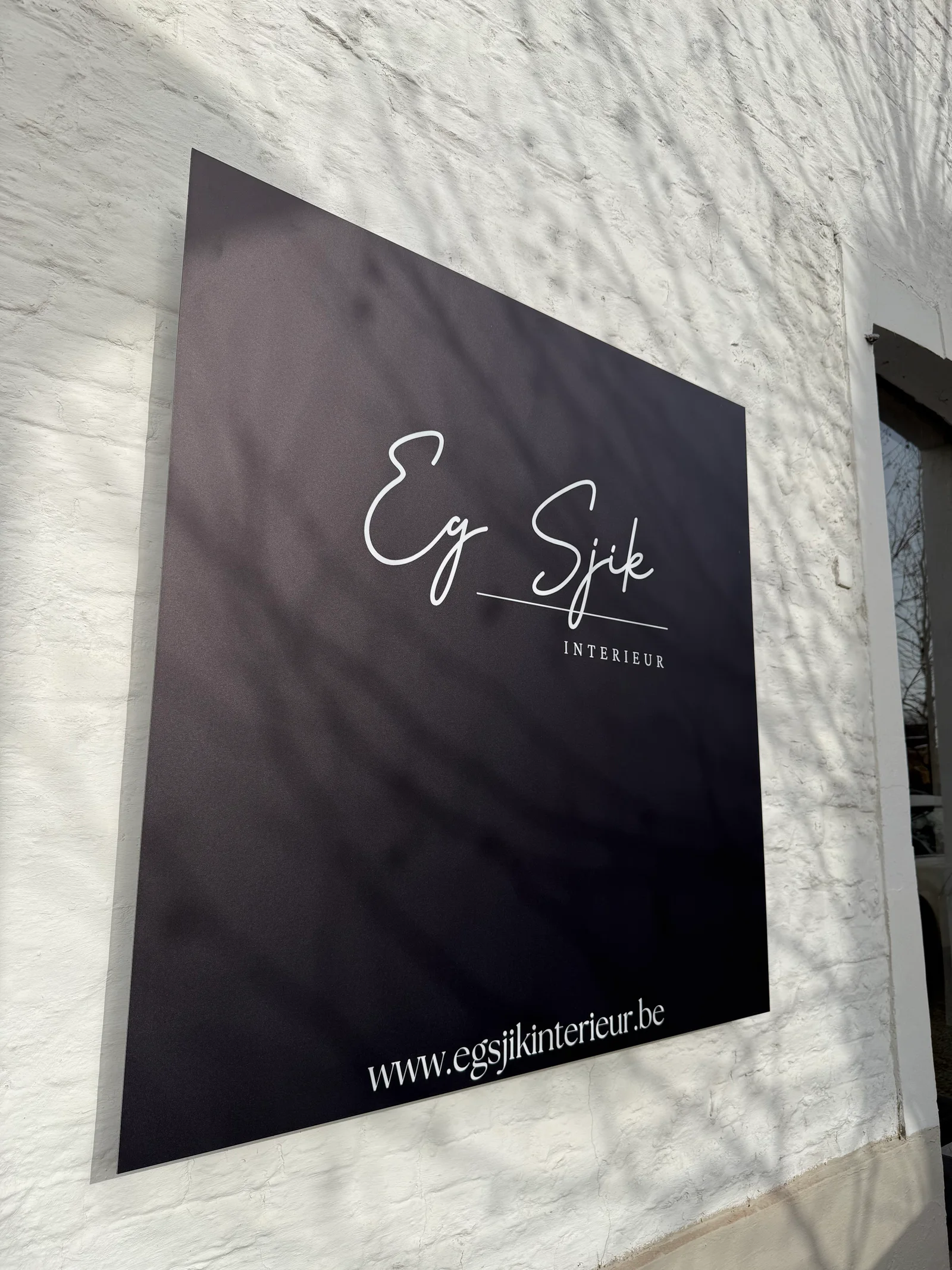 Zwart aluminium reclamebord van Eg Sjiek Interieur gemonteerd op een witte gevel